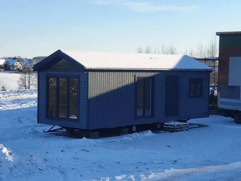 Winterfestes Mobilheim von Compact Haus in Graublau mit Satteldach und sichtbarer Deichsel in winterlicher Umgebung.