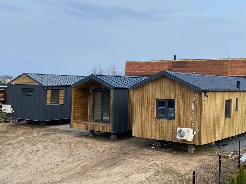 Mehrere winterfeste Mobilheime der MONO-Serie von Compact Haus mit Holzfassade, Klimaanlage, überdachter Terrasse und anthrazitfarbenem Satteldach auf einem Stellplatz.