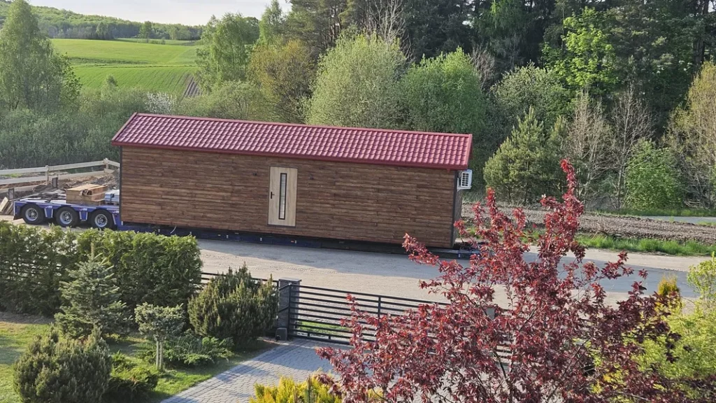 Anlieferung eines winterfesten Modulhauses der MONO-Serie von Compact Haus mit Holzfassade und rotem Satteldach auf einem Tieflader für die deutschlandweite Lieferung.