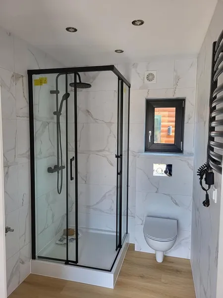 Helles Badezimmer in einem winterfesten Modulhaus der MONO-Serie von Compact Haus mit Marmoroptik-Fliesen, Glasdusche und Design-Heizkörper.