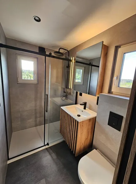 Stilvolles Badezimmer in einem winterfesten Modulhaus der MONO-Serie von Compact Haus mit barrierefreier Walk-In-Dusche, Marmoroptik-Fliesen und beleuchtetem Spiegelschrank.