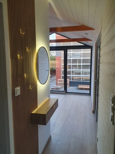 Moderner Eingangsbereich im skandinavischen Loft-Stil in einem winterfesten Modulhaus der MONO-Serie von Compact Haus mit Garderobenwand aus Holzlamellen und LED-Spiegel.