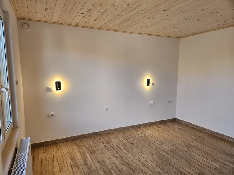 Heller Wohnraum im skandinavischen Stil in einem winterfesten Modulhaus der MONO-Serie von Compact Haus mit Echtholzdecke, Wandleuchten und Holzoptikboden.