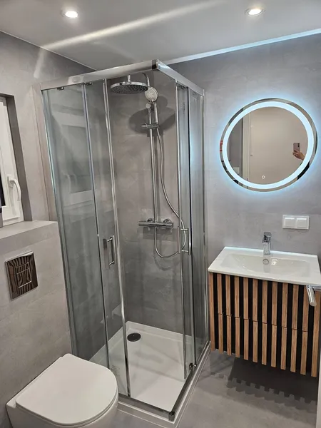 Modernes Badezimmer in einem winterfesten Tiny House der MONO-Serie von Compact Haus mit Glasdusche, rundem LED-Spiegel und Holzwaschtisch in Lamellenoptik.