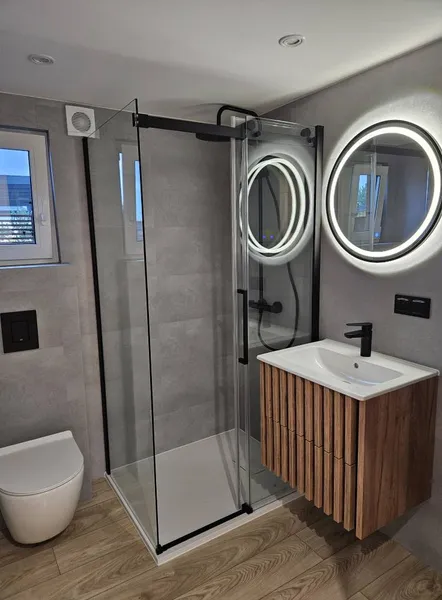 Modernes Luxus-Badezimmer in einem winterfesten Tiny House der MONO-Serie von Compact Haus mit Eck-Glasdusche, rundem LED-Spiegel und hochwertigem Holzwaschtisch.