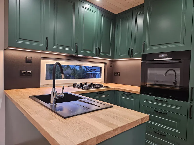 Hochwertige Einbauküche im Landhausstil mit waldgrünen Kassettenfronten, einer hellen Massivholzarbeitsplatte und einem integrierten Gasherd in einem Tiny House der MONO-Serie.