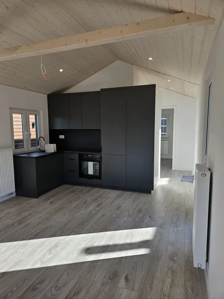 Moderne, grifflose Einbauküche in Mattschwarz unter einer hohen, hellen Giebel-Holzdecke mit Einbaustrahlern in einem Tiny House der MONO-Serie.