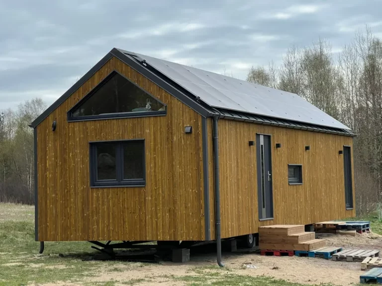 Winterfestes Tiny House der MONO-Serie von Compact Haus in Holzständerbauweise mit Solaranlage, markantem Giebelfenster und natürlicher Holzfassade auf Trailer-Fahrgestell.