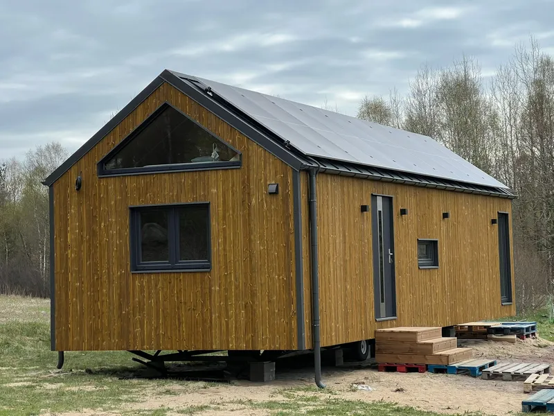 Winterfestes Tiny House der MONO-Serie von Compact Haus in Holzständerbauweise mit Solaranlage, markantem Giebelfenster und natürlicher Holzfassade auf Trailer-Fahrgestell.
